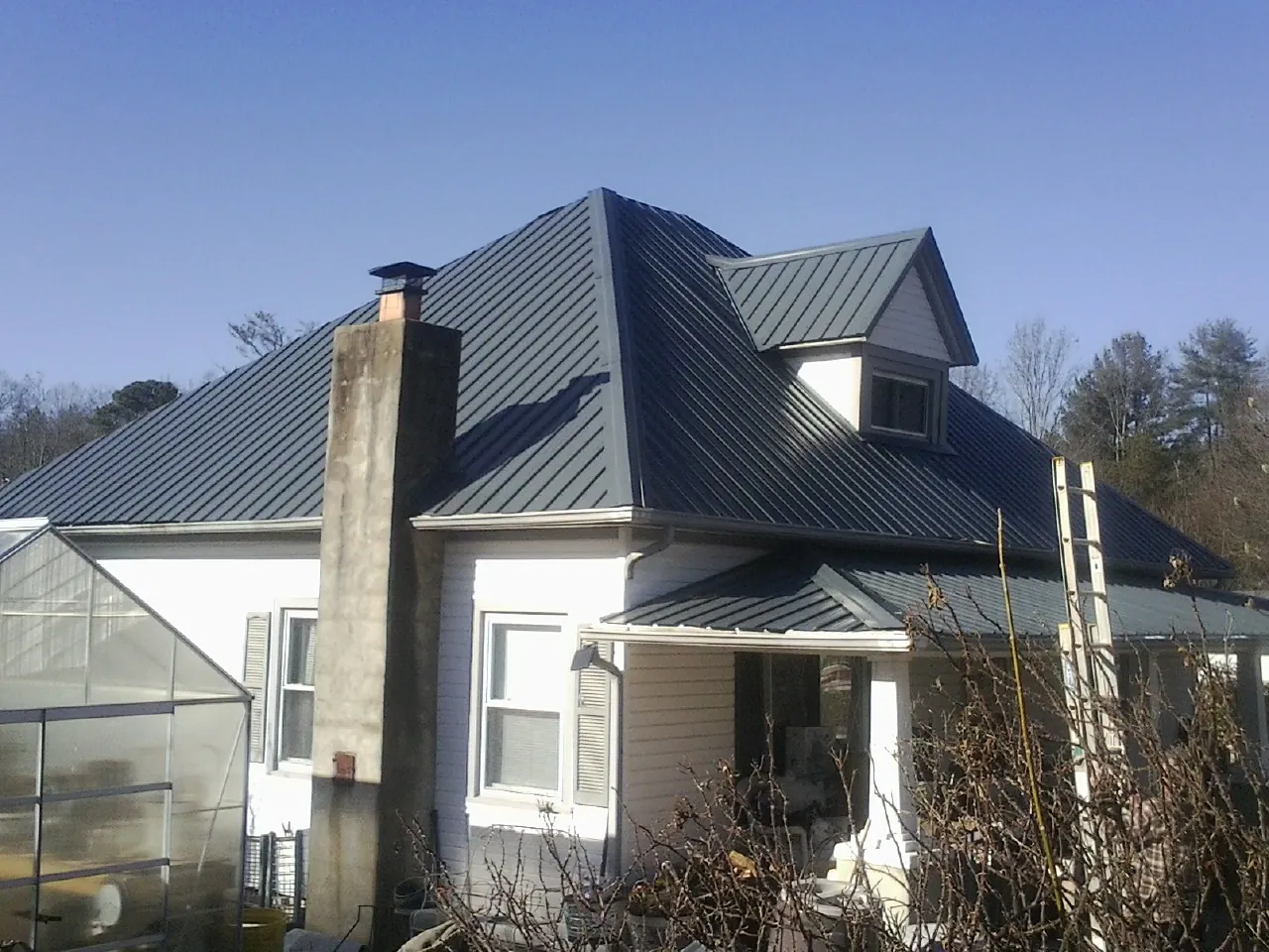 Dark blue standing seam metal roof on a white farmhouse with dormer — Slate & Tile Roof Repair by Roofing Brothers in Cumbola