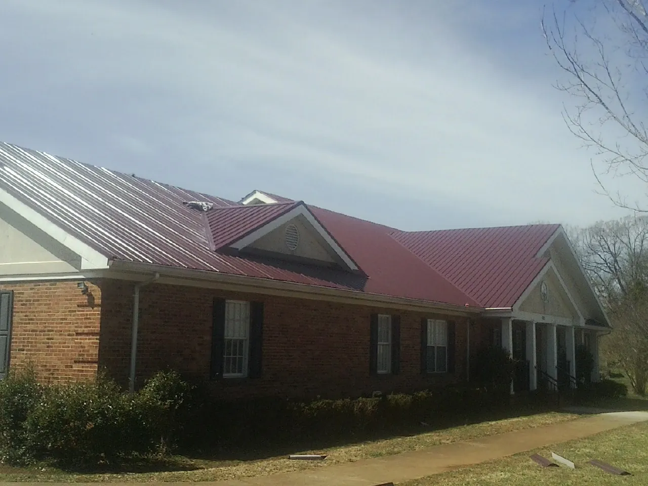 Red metal roof with gabled entries on a long brick building, from a Hail Damage Roof Repair job in Cumbola