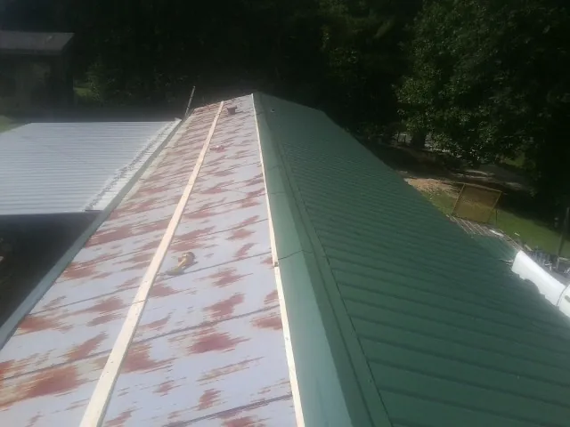 Old rusted panels beside newly installed green metal roofing — Wind Damage Roof Repair by Roofing Brothers in Cumbola