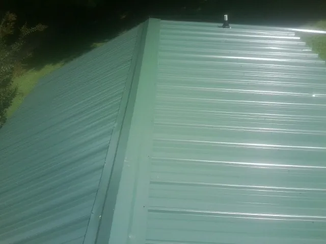 New green metal panels meeting at the ridge of a roof — Flat Roof Repair work by our crew in Cumbola