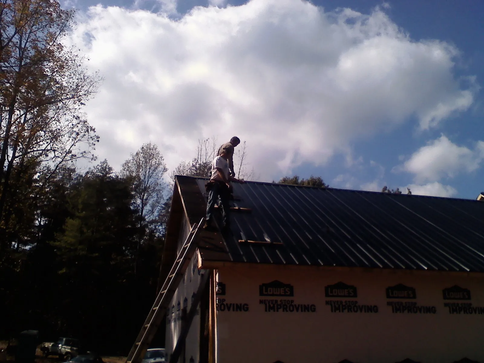 Roofer fastening dark metal panels high against a cloudy sky, from a Roof Inspection job in Cumbola