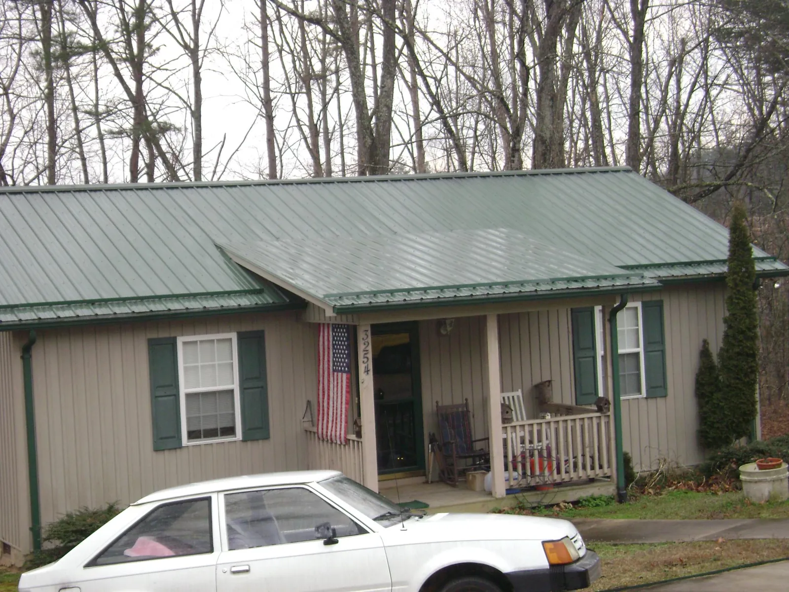 Green metal roof and front porch on a tan sided cottage in Cumbola