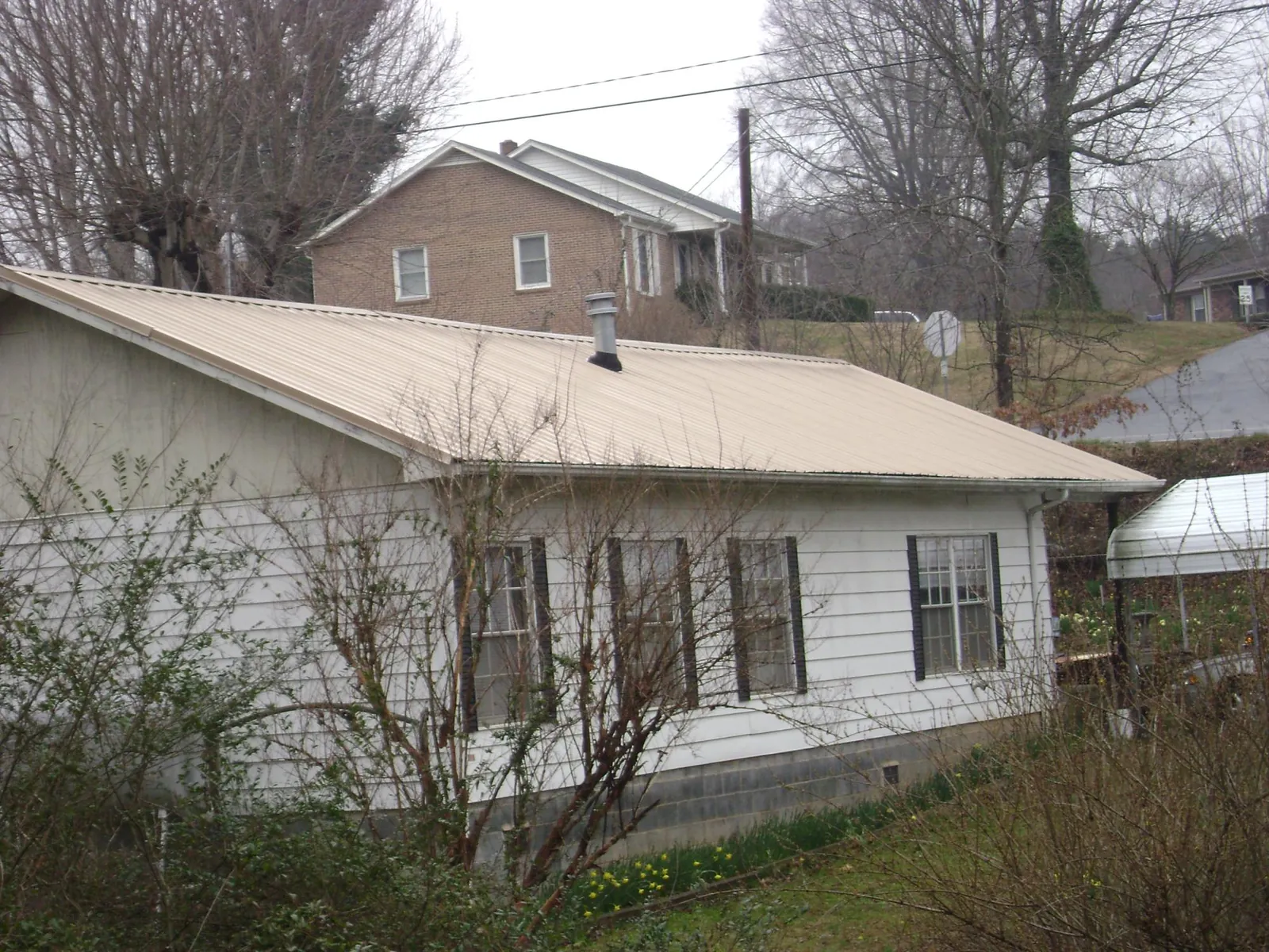 Tan metal roof on a white sided house set into a hillside — Commercial Roofing by Roofing Brothers in Cumbola