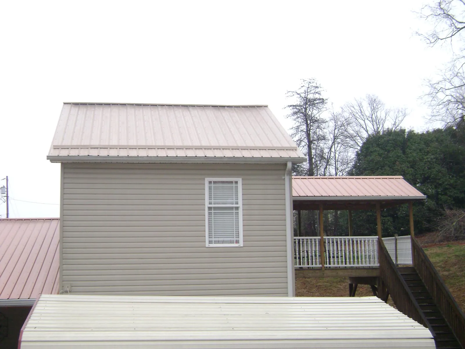 Tan metal roofs on a two story addition and attached porch, from a Roof Replacement job in Cumbola