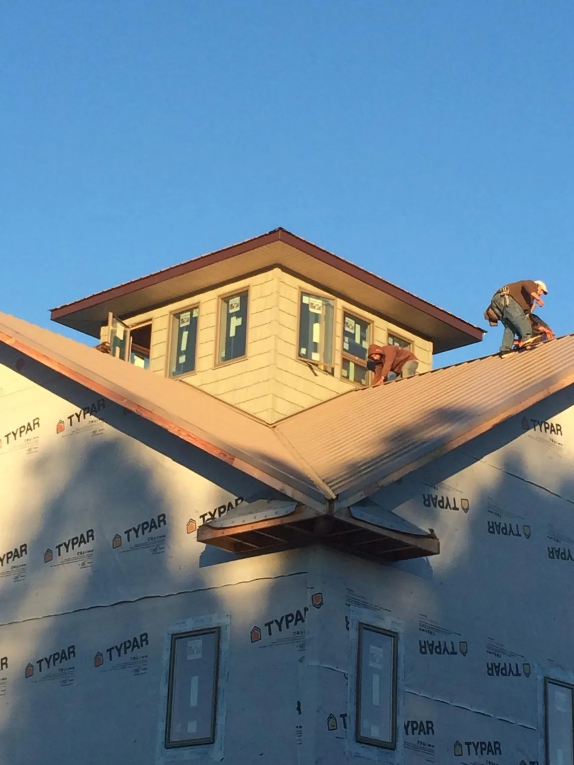 Roofers working around a rooftop cupola on a new metal roof at sunset — Roof Waterproofing in Cumbola by Roofing Brothers